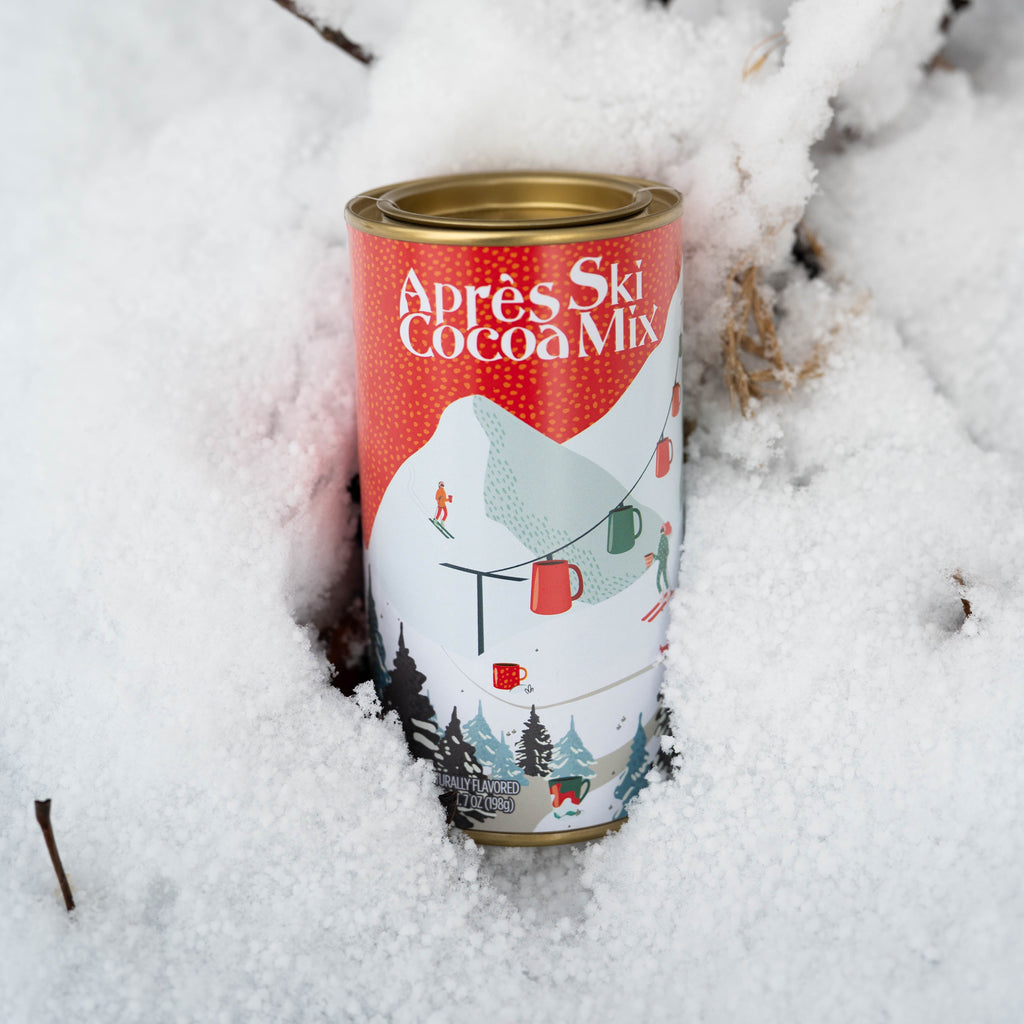 Can of Après Ski Cocoa Mix surrounded by snow and branches