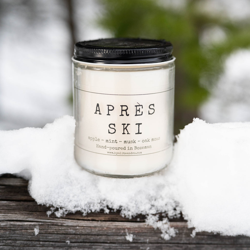 Candle labeled 'Apres Ski' on a snowy surface with a blurred natural background