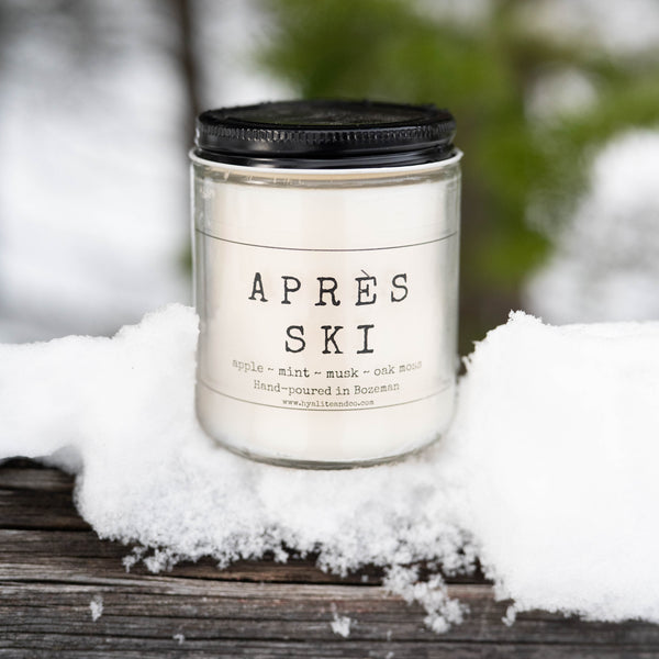 Candle labeled 'Apres Ski' on a snowy surface with a blurred natural background