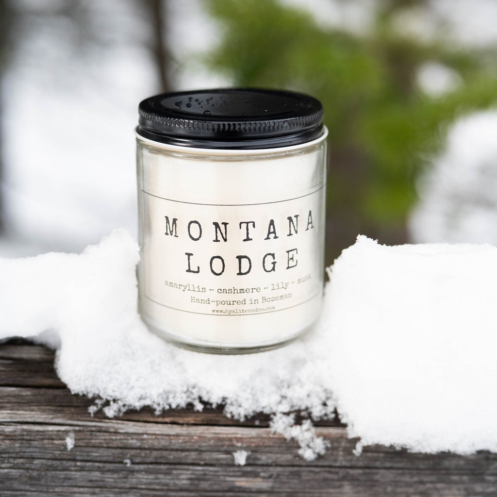Candle labeled 'Montana Lodge' on a snowy surface with blurred natural background