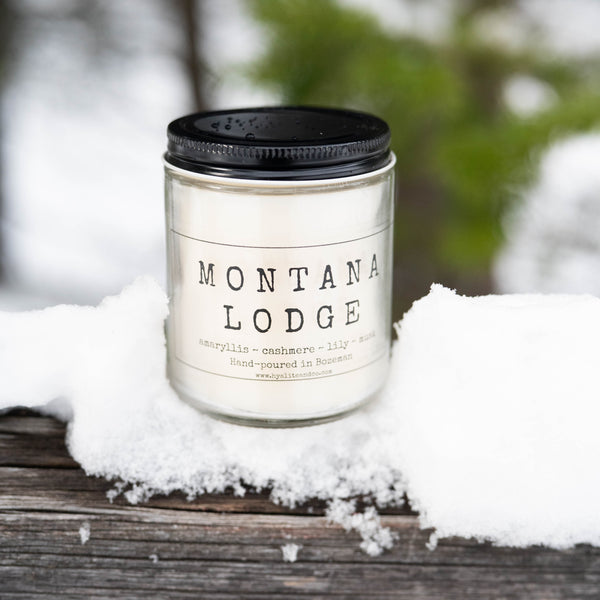 Candle labeled 'Montana Lodge' on a snowy surface with blurred natural background